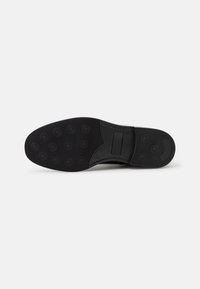 Suela de zapato de goma negra con un patrón de agarre texturizado que combina elementos circulares y lineales; diseño plano con punta redondeada.