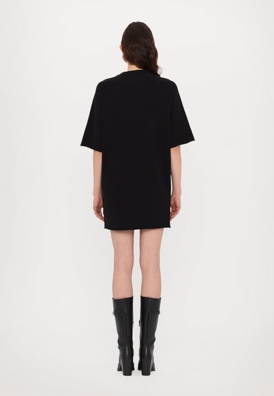 Vestido de camiseta negro de gran tamaño con mangas cortas, dobladillo recto, detalle de costura mínima y combinado con botas negras de tacón alto hasta la rodilla.