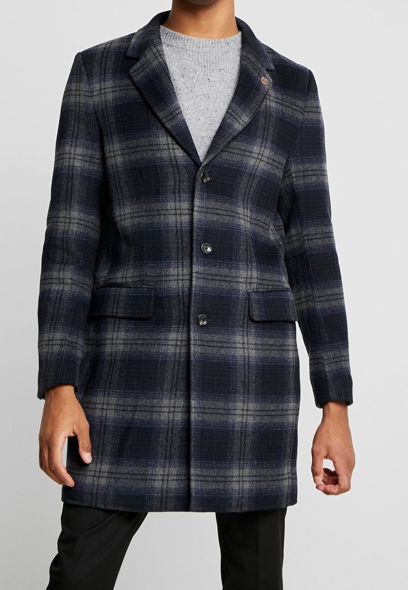 Cappotto in misto lana a quadri nei colori blu navy, grigio e nero. Presenta un colletto a revers, due tasche frontali e una chiusura con bottone singolo.