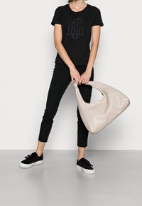 Sort bomulds T-shirt med logo, parret med sorte slim pants og sorte sneakers. Har en beige læder hobo taske med et buet håndtag.