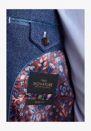 Herringbone-patterned navy fabric blazer with a floral burgundy lining, featuring a brown button and a label stating "next SIGNATURE, SLIM FIT."