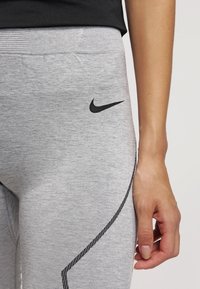 Szare legginsy sportowe z czarnym logo Nike, gładka faktura, dopasowany krój i kontrastowe przeszycia po bokach.