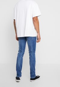 Bílé tričko s kulatým výstřihem, krátké rukávy, v kombinaci se světle modrými úzkými džínami a černými teniskami s bílými detaily. Jednoduchý a ležérní vzhled.