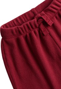 Burgunderfarbene gerippte Jogginghosen mit elastischem Bund und gebundenem Schleifchen, die einen strukturierten Stoff und eine lockere Passform zeigen.