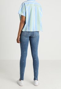 Ljusblå randig kortärmad skjorta, i kombination med tighta mörkblå jeans med blommig broderi och vita sneakers.