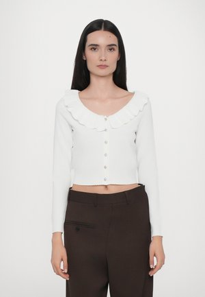 Vit kort cardigan med en böljande, vågig krage, långa ärmar och knäppningar med dekorativa detaljer.