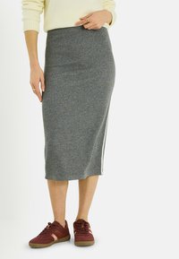 Falda midi de punto gris con ajuste ceñido y abertura lateral, combinada con zapatillas burdeos. La tela tiene un aspecto texturizado y un diseño cómodo.