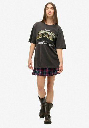 Czarny oversize t-shirt z metalicznym wzorem, w zestawieniu z krótką spódnicą w kratę w czerwono-niebieskie wzory oraz kozaki z czarnej skóry do kolan.