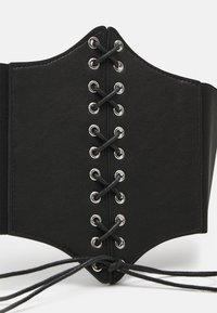 Black corset with a structured shape, featuring metal grommets and laces in the center, and elastic side panels for stretch and fit.