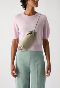 Svetloružový sveter s krátkym rukávom, zelené pruhované nohavice a jemná béžová crossbody taška so zhlukovaným dizajnom a šnúrkovým zapínaním.