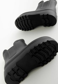 Bottes de cheville en caoutchouc noir avec une surface texturée et une semelle à motif rugged pour une meilleure adhérence. Présente un design à enfiler avec des accents élastiques.