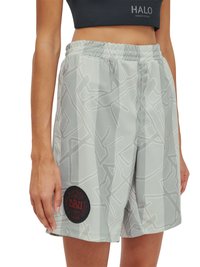 Kobieta nosząca jasnoszare szorty z abstrakcyjnymi wzorami linii oraz czarną, okrągłą naszywką z logo DBU na lewej nodze, w połączeniu z czarnym crop topem.