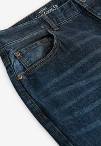 Jeans de mezclilla azul oscuro con un diseño de pierna recta, que presentan un lavado medio, costuras en cobre y detalles en los bolsillos frontales.