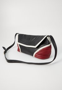 Læder skuldertaske med en sort top og front, hvide accenter og en tekstureret rød bund. Har en lang sort rem og trekantede design detaljer.