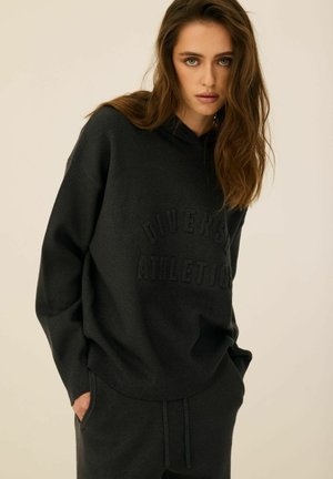 Czarna bluza z kapturem z wytłoczonym napisem "DIVERSITY ATHLETIC". Wykonana z miękkiego materiału, z luźnym fasonem i kieszeni�ą z przodu. Stylizowana z dopasowanymi spodniami.