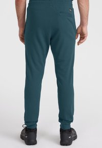 Turkusowe spodnie dresowe z miękkiego materiału, z tylną kieszenią i elastycznymi mankietami, w zestawie z czarnymi butami sportowymi.