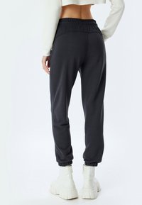 Mørkegrå joggere med elastisk talje og manchetter, lavet af et blødt stof, parret med hvide støvler med kraftige såler.