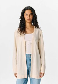 Cardigan beige aperto realizzato in materiale knit leggero, con strisce verticali testurizzate, maniche lunghe e polsini a coste.