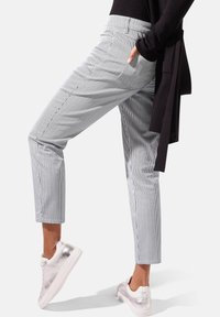 Grijze en witte gestreepte broek met een getailleerde pasvorm, enkelhoogte en zijzakken, gecombineerd met metallic zilveren sneakers.