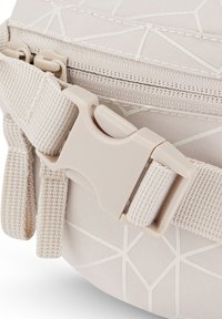 Gros plan d’un sac en tissu beige avec une boucle latérale en plastique et un motif géométrique sur le matériau.