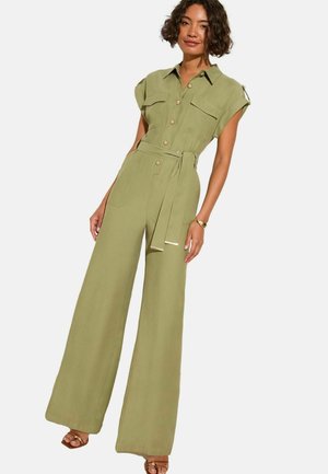 Tuta utility verde con maniche corte, tasche oversize, vita con cintura e pantaloni a gamba larga. Presenta bottoni e rifiniture dorate.