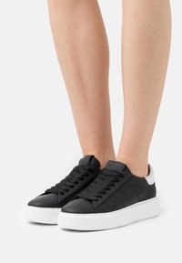 Czarne skórzane sneakersy z białą gumową podeszwą, z teksturowanym sznurowaniem i kontrastującym białym akcentem na pięcie.