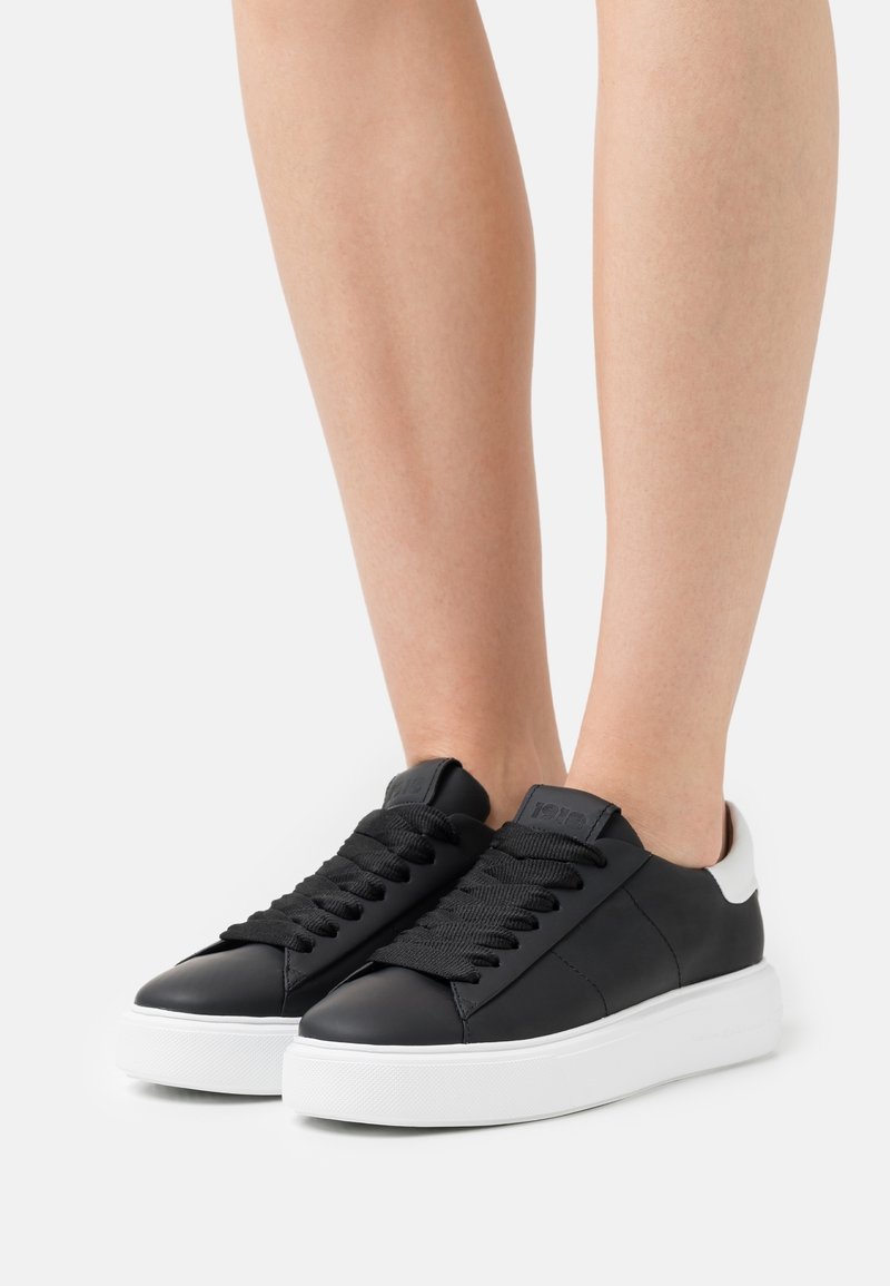 Czarne skórzane sneakersy z białą gumową podeszwą, z teksturowanym sznurowaniem i kontrastującym białym akcentem na pięcie.