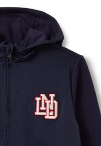 Chaqueta con capucha en color marino, con cierre de cremallera y un gran logotipo bordado "ND" en rojo y blanco en el pecho. Textura suave, diseño casual.