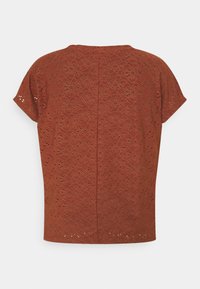 Haut à manches courtes couleur rouille avec un motif floral découpé au laser, un col rond et une coupe droite, avec une texture de tissu lisse.