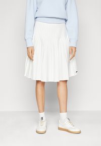 White pleated skirt with a high waistband, paired with a light blue sweatshirt and white sneakers featuring a textured sole.