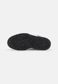 Semelle d'une basket noire Puma avec des motifs de crampons circulaires et triangulaires et le logo Puma au centre.