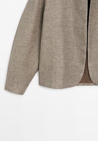 Světlý hnědý strukturovaný blejzr s dlouhým rukávem a otevřeným předním dílem, ukazující sladěnou vnitřní podšívku na bílém pozadí.