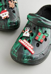Crocs negre și verzi cu marmură, prezentând pini decorative tematice de sărbători: om de zăpadă, cadou, ren și un, badge cu mesajul "Crăciun Fericit".