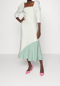 Robe colorée en blocs blanc et menthe avec des manches bouffantes et un décolleté carré, dotée d'un ourlet fluide. Escarpins roses à bout pointu avec des accents ronds.