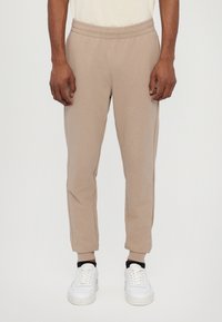 Beige joggerbroeken van zachte stof, met een elastische tailleband met trekkoord, elastische boorden en zijnaaddetails. Draag het met witte sneakers.