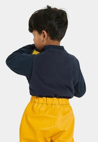 Marineblauwe fleece pullover met een hoge kraag, gecombineerd met felgele broek met elastische taille. De stoffen lijken zacht en gestructureerd.