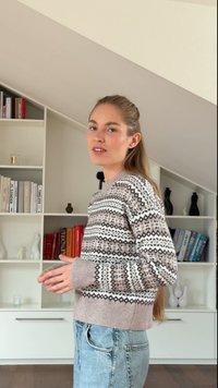 Suéter de punto con patrones geométricos en tonos marrones y blancos; puños y dobladillo acanalados; combinado con jeans de mezclilla claros; fondo minimalista.