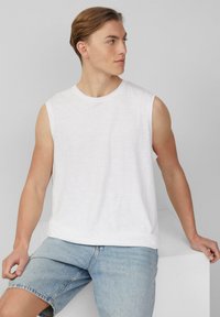 Witte katoenen mouwloze T-shirt met een ronde hals, gecombineerd met lichtblauwe denim shorts. Eenvoudig ontwerp, zachte textuur, geen zichtbare logo's.