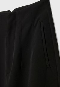Gros plan d’un pantalon noir sur mesure montrant la couture latérale et le détail de la poche fendue verticale.