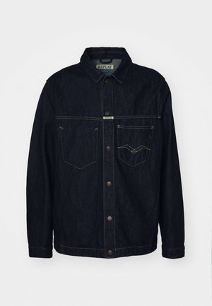 Giubbotto di jeans scuro con colletto a camicia, due tasche sul petto e chiusura con bottoni. Presenta cuciture gialle a contrasto e un'etichetta con il marchio.