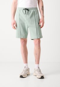Shorts vert menthe avec une taille élastique et un cordon noir, dotés de poches latérales et d'un détail de logo sur la cuisse gauche.