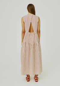 Abito maxi a righe in crema e rosso, con schiena a chiave, vita arricciata e una silhouette fluida. Si abbina a sandali con tacco rossi.