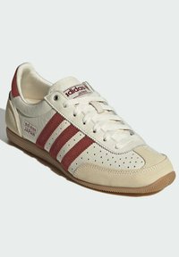 Adidas Japan tenisice sa kremastom kožnom površinom, crvenim nubuk trakama, perforiranim detaljima sa strane i gumenim potplatom.