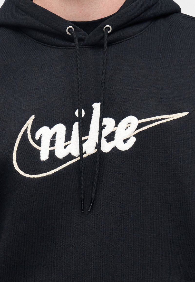 Black hoodie featuring a large white embroidered "nike" logo. Drawstrings with aglets, soft texture, and a relaxed fit design.