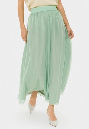 Gonna maxi di un verde menta trasparente con cintura elastica, caratterizzata da un tessuto morbido e fluente e una silhouette ampia. Scarpe argentate a punta brillanti.