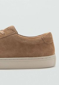 Tan suede kengät, joissa on ommeltu yksityiskohta ja beige kumipohja, esitetty sivulta neutraalin taustan edessä.
