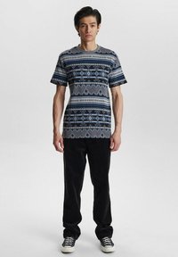 Camiseta de manga corta en gris con patrones geométricos en azul y negro, combinada con pantalones negros y zapatillas negras.
