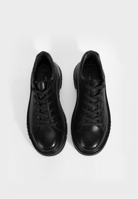 Baskets en cuir noir avec un bout arrondi, des lacets proéminents, des accents texturés et une semelle rembourrée. Vue de haut mettant en valeur les détails du design.