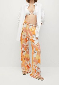 Pantalon large fluide à motifs floraux dans des nuances d'orange et de blanc, avec une taille à cordon. Associé à une chemise blanche ample et des sandales.