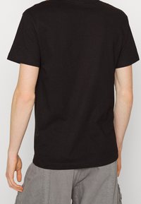 Camiseta negra de manga corta con cuello redondo, hecha de algodón, que presenta una textura suave y un diseño simple, sin adornos.